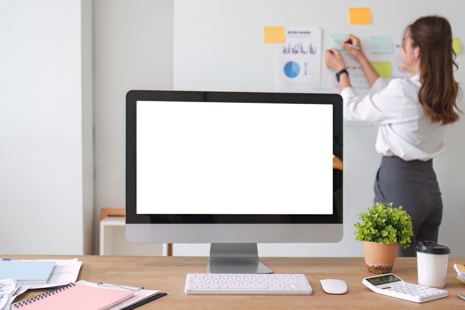 Modern work desk with computer open screen on white In the background, business people are planning their work on the board, financial and marketing reports, calculators and supplies.